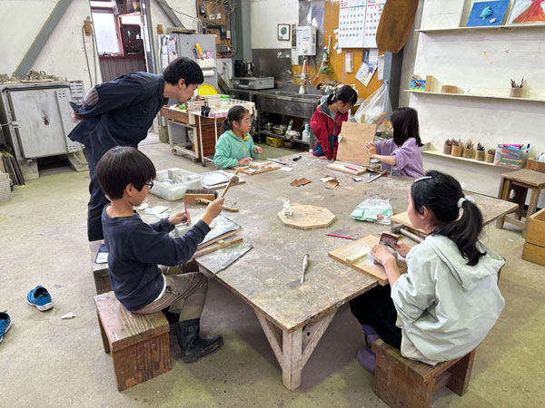大きな机を子どもたちが囲み図工の授業をしている